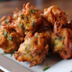 Hare Krishna vegetable pakoras served on a white plate with lemon wedges, featuring crispy golden chickpea batter and fresh herbs.